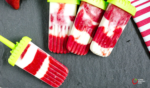 overhead view of strawberry creamsicles on a dark background with green popsicle sticks