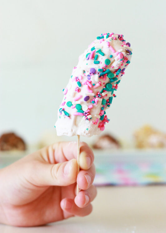 frozen banana pop held by a child covered in yogurt and sprinkles