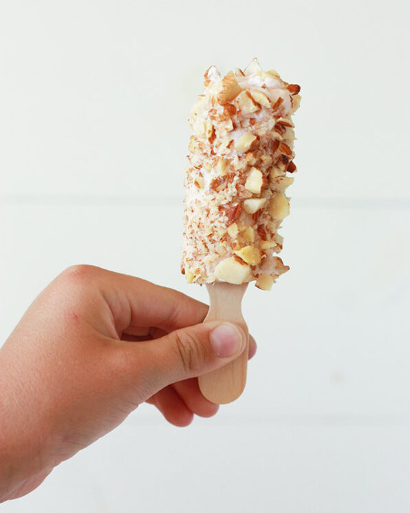 frozen banana pop held by a child covered in yogurt and nuts