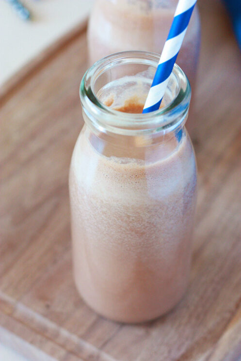 homemade chocolate milk in a milk glass with a blue and white striped straw