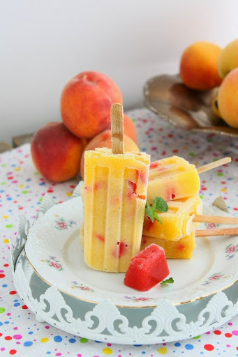 strawberry peach popsicles with a stack of fresh peaches in the background