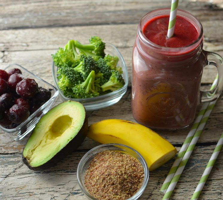 broccoli smoothie in a jar with a striped straw on a table with broccoli, avocado, banana and cherries