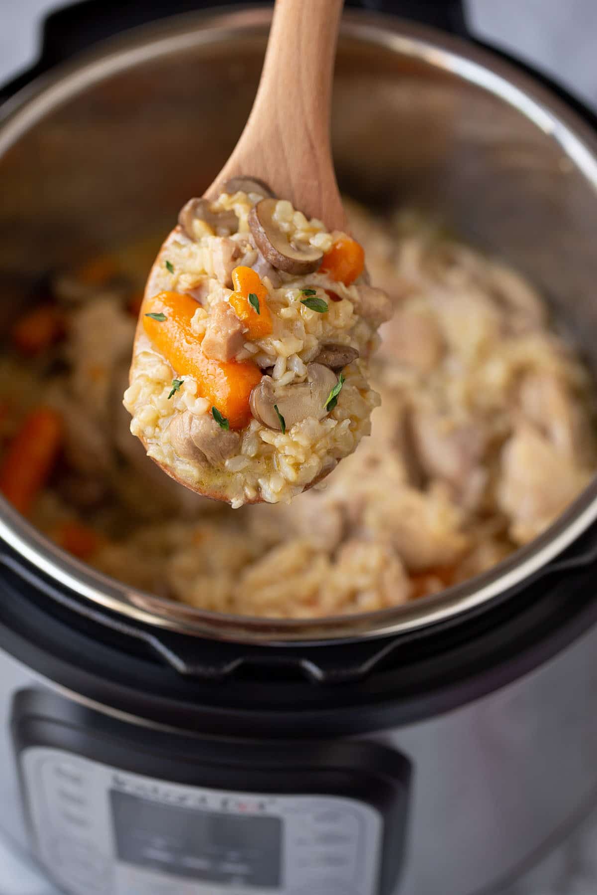 instant pot chicken and brown rice dinner on a wooden spoon over the instant pot