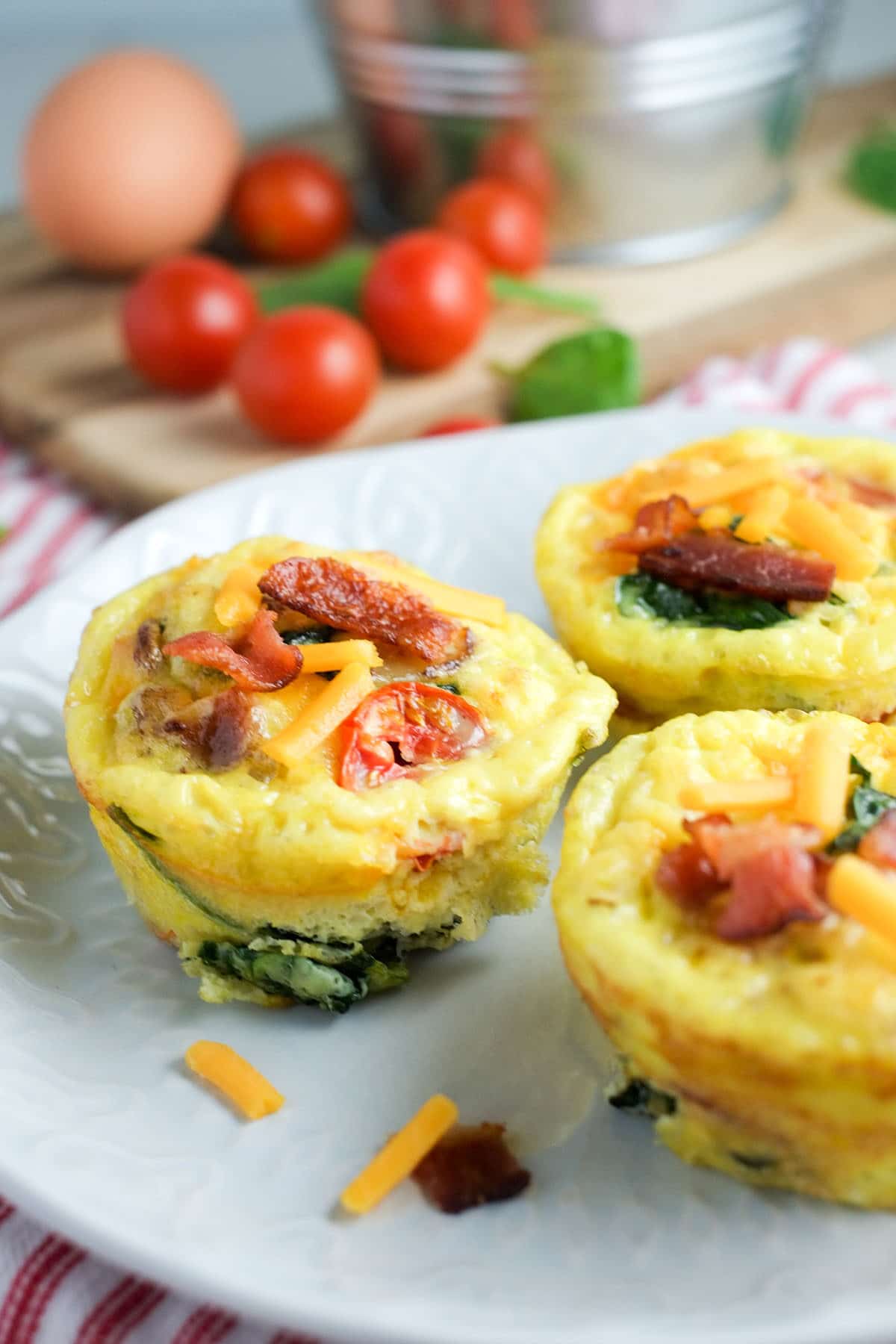 egg muffin cups with tomatoes, bacon and spinach on a white plate