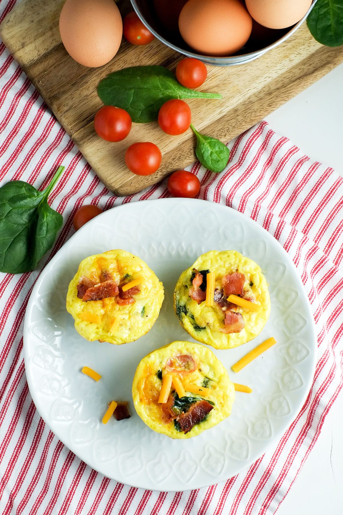 cherry tomatoes, spinach and egg muffin cups on a white plate with a red and white striped napkin underneath