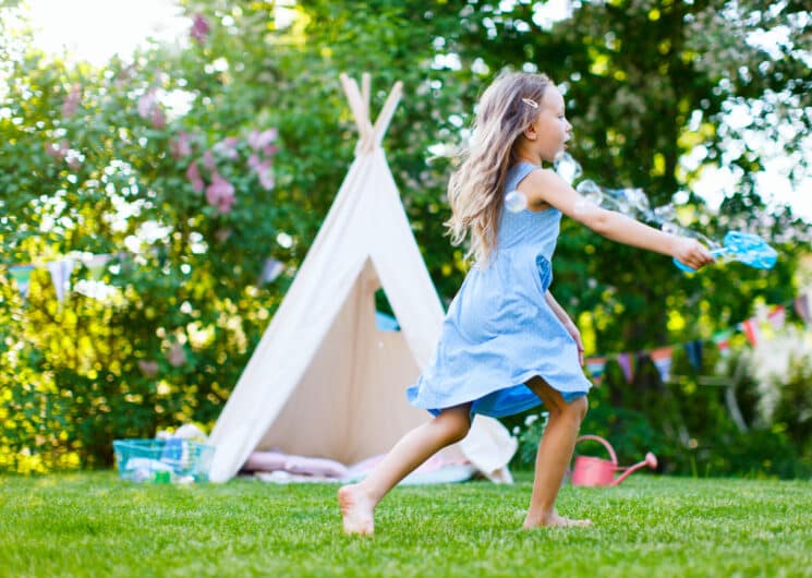girl playing with bubbles outdoors on the grass with a play tent in the background