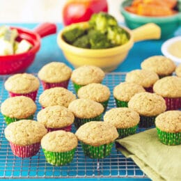 fruit and veggie muffins on a cooling rack with vegetables in the background in colorful bowls