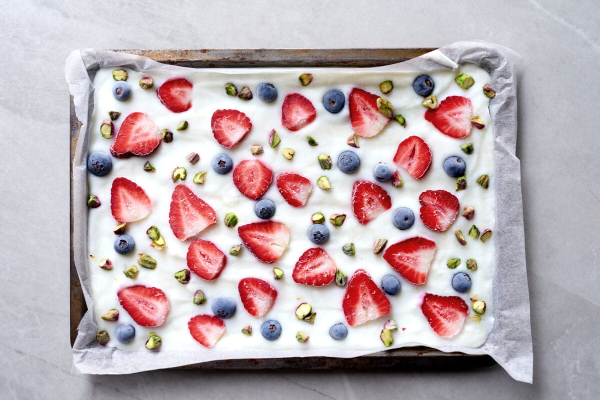 frozen yogurt bark on a parchment lined tray topped with strawberries, blueberries, and pistachios