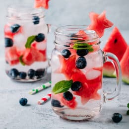 fruit infused water with watermelon stars, blueberries and mint in a glass mason jar with watermelon slices in the background