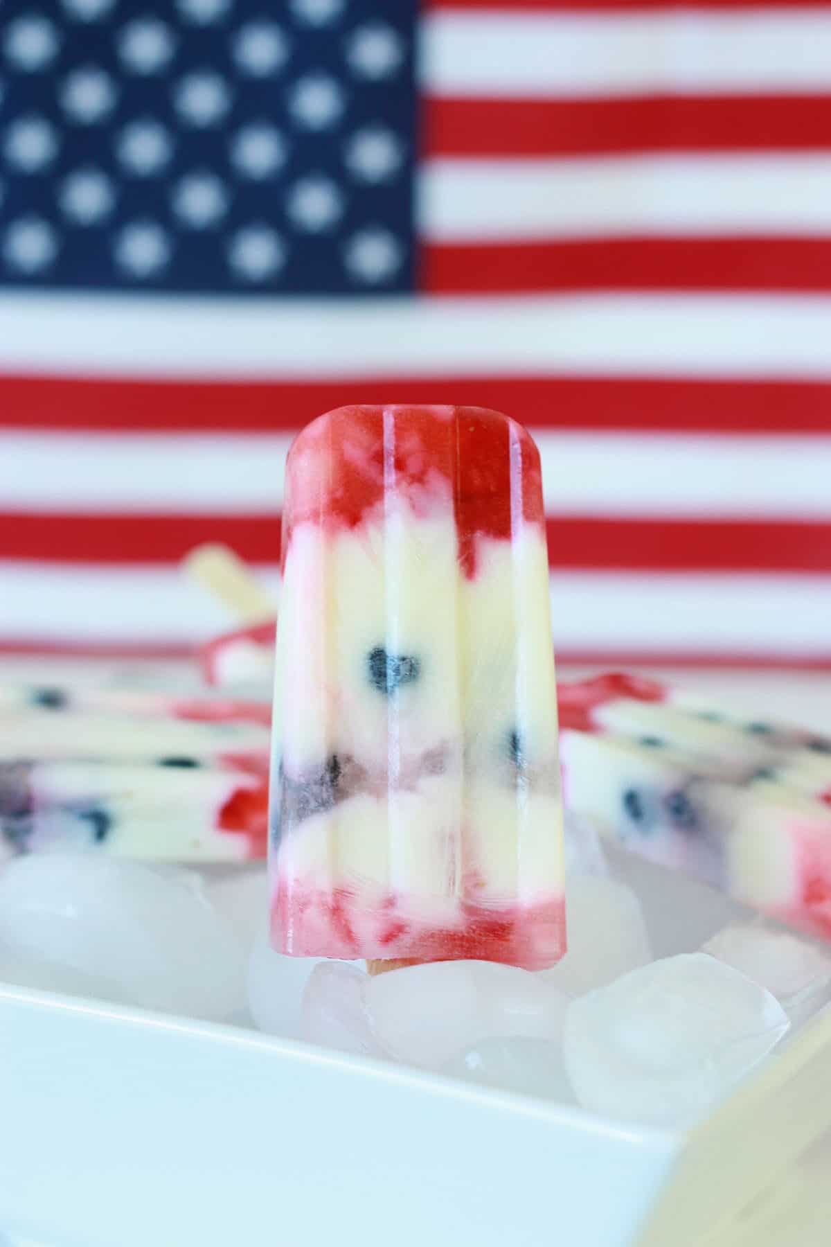 red white and blue popsicle with healthy ingredients in a bowl of ice with an american flag in the background