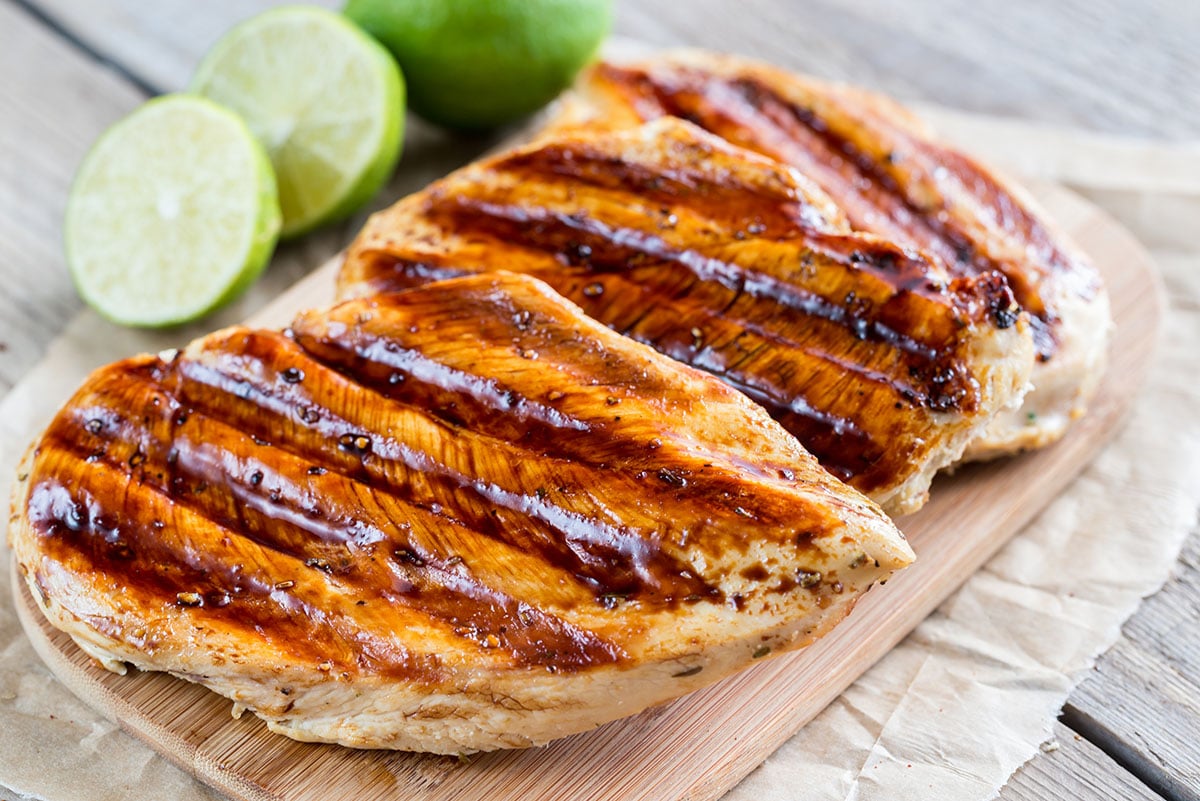 grilled chicken breast with a coconut lime marinade on a wooden cutting board with fresh limes in the background