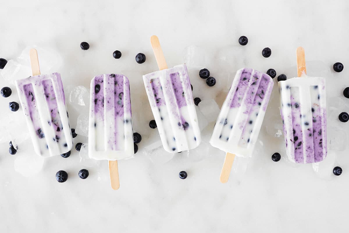 Group of blueberry popsicles. Above view in a row on a white marble background.