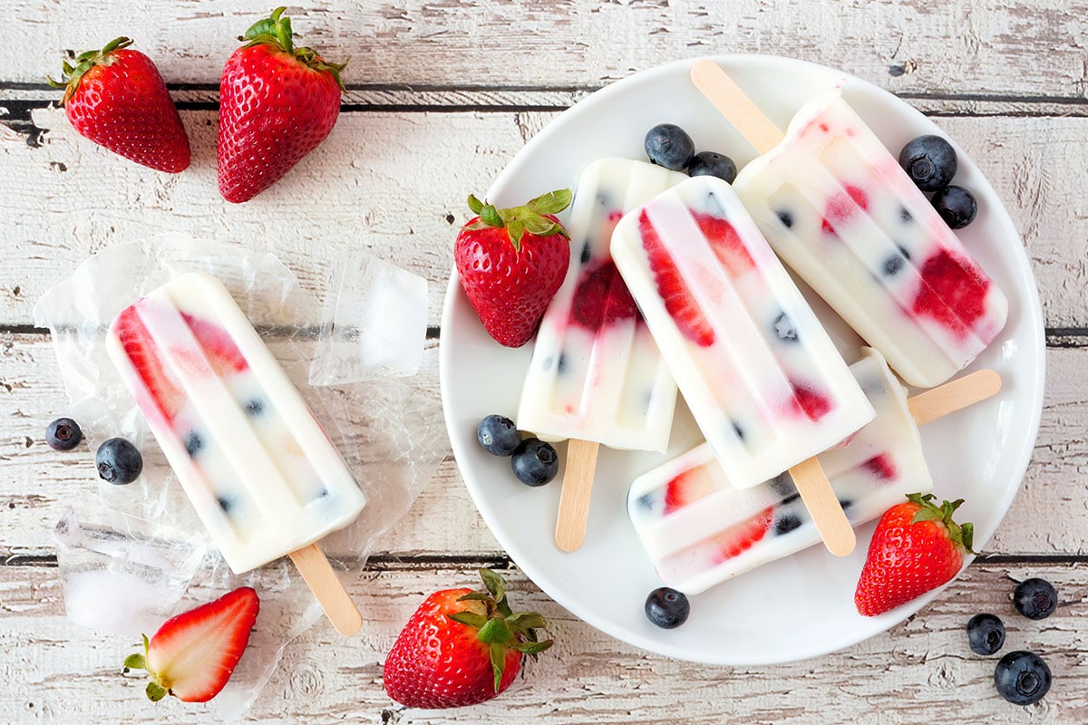 Healthy strawberry blueberry yogurt popsicles on a plate, above view summer table scene against a white wood background