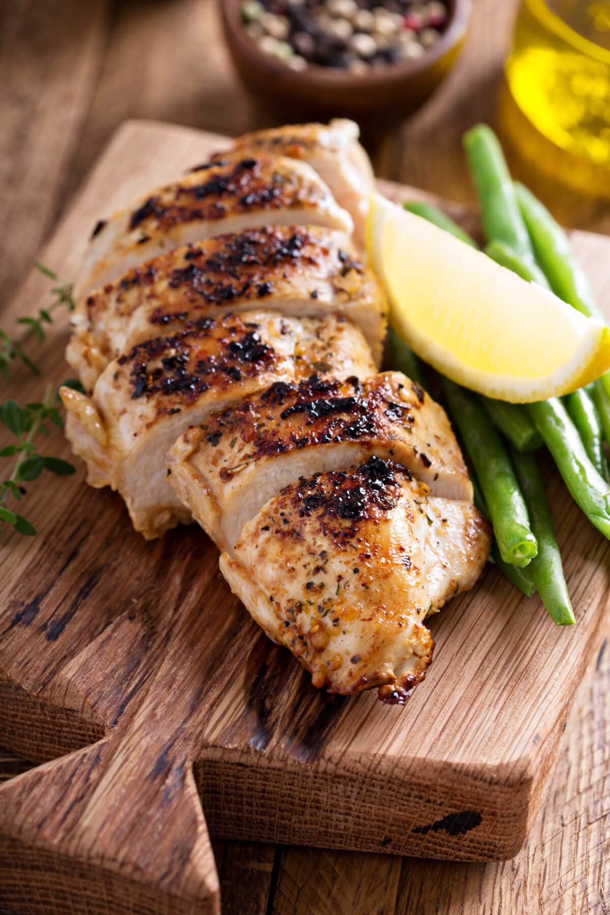 Grilled lemon chicken on a cutting board with thyme and green beans