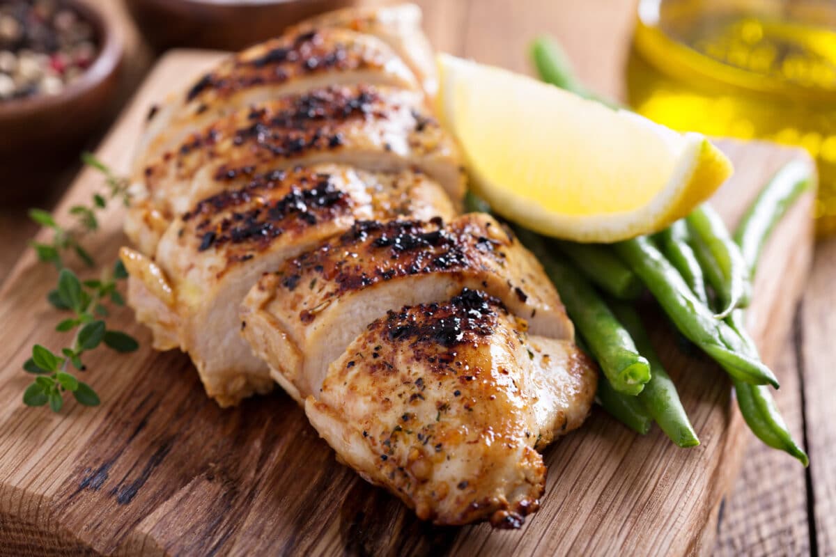 Grilled lemon  chicken on a cutting board with thyme and green beans