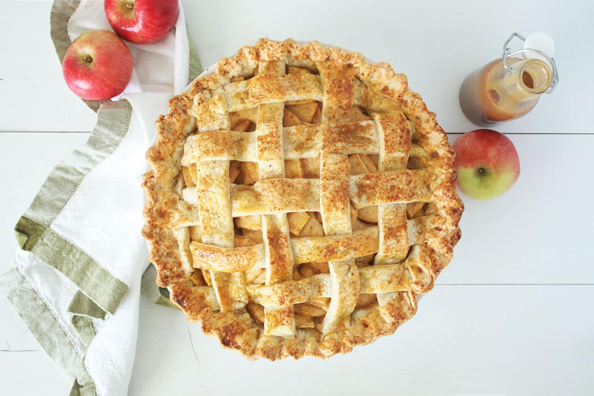 an apple pie with a lattice crust with apples in the background