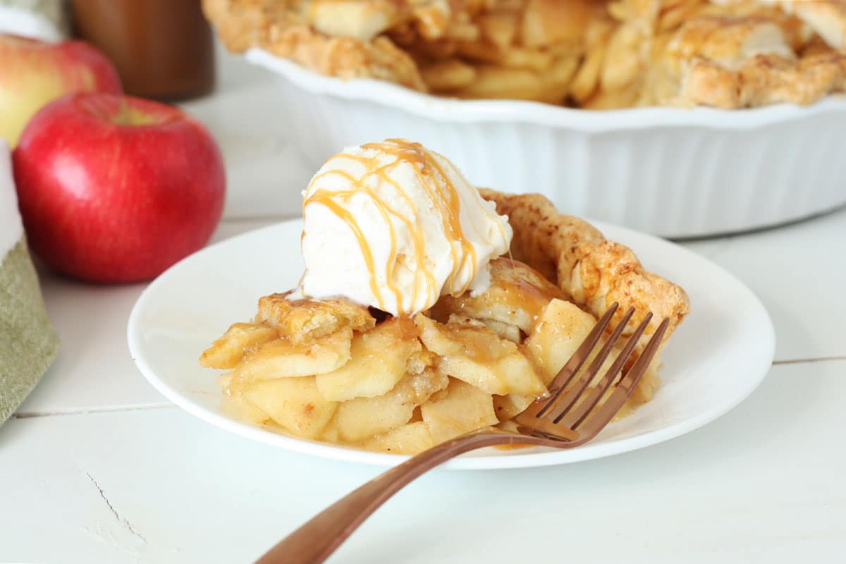 slice of caramel apple pie topped with vanilla ice cream and caramel sauce