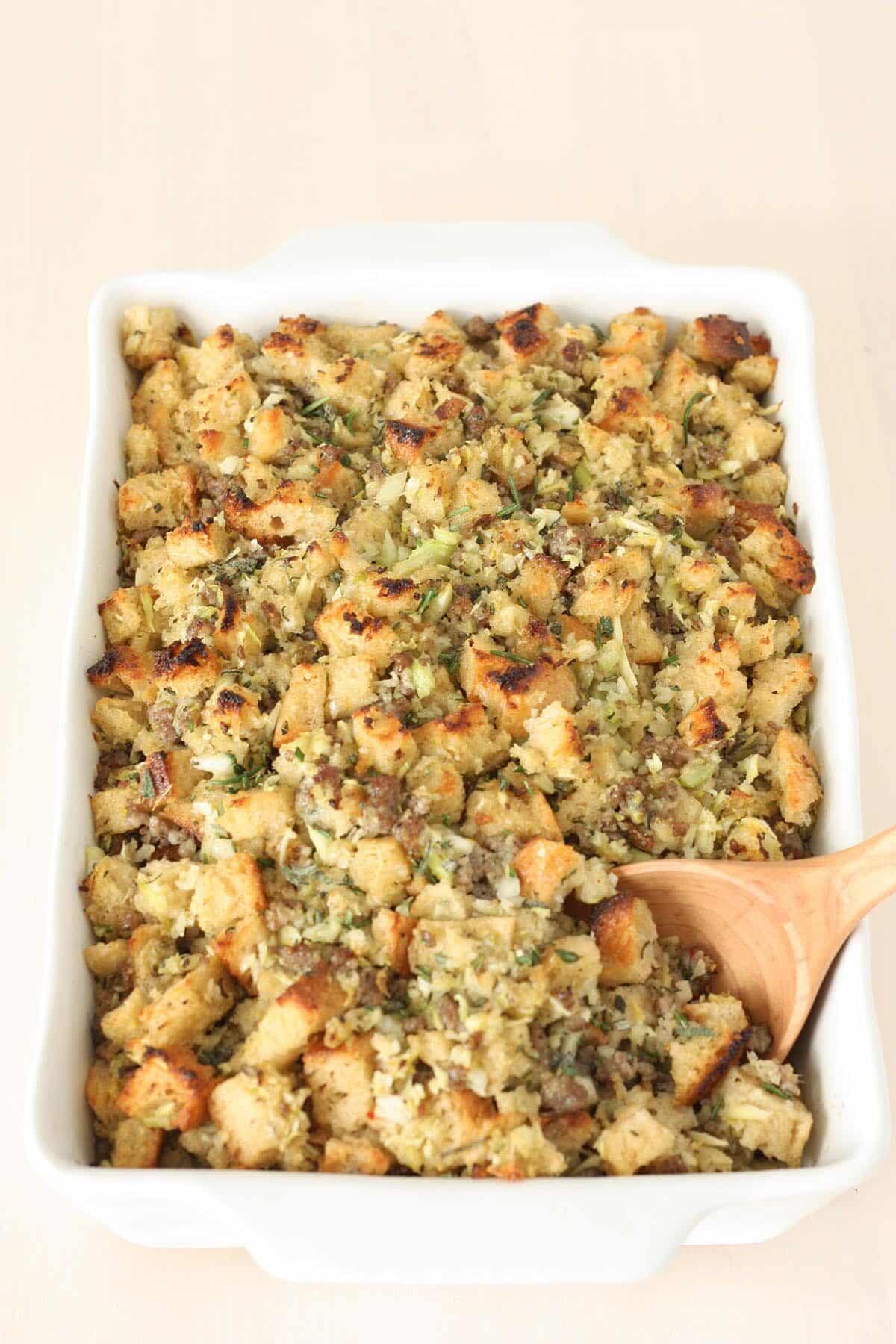 baked homemade stuffing in a white casserole dish with a wooden spoon