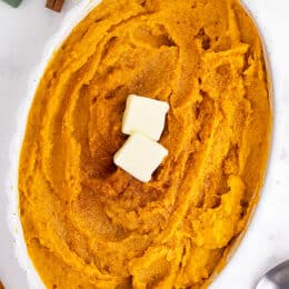 mashed sweet potatoes in a white dish with pats of butter on top