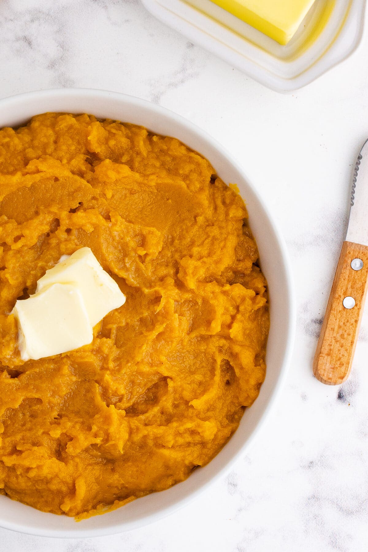 overhead view of a bowl of mashed sweet potatoes with a pat of butter on top