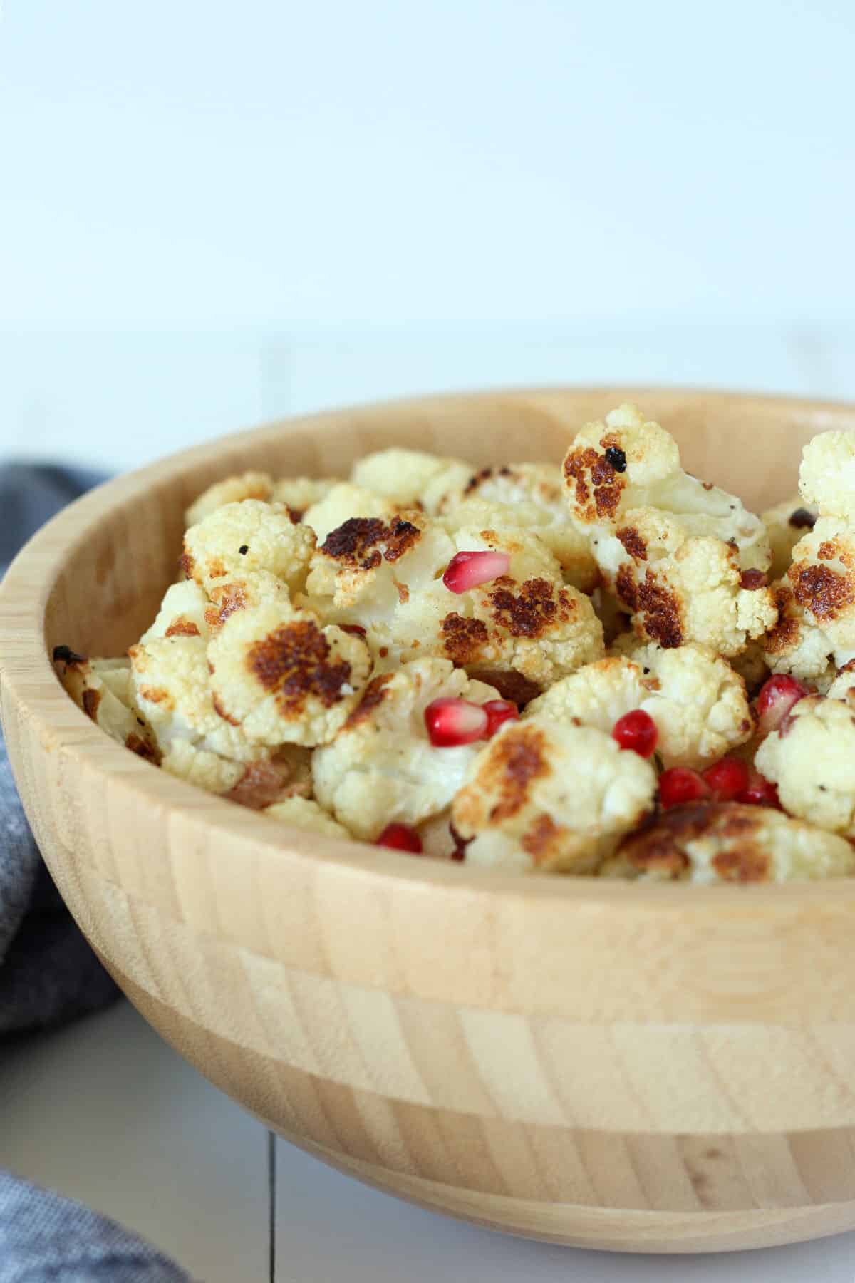 closeup view of a bowl of roasted cauliflower with pomegranate arils and bacon pieces