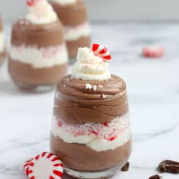 chocolate peppermint mousse in a clear glass with whip cream and peppermint candy garnish