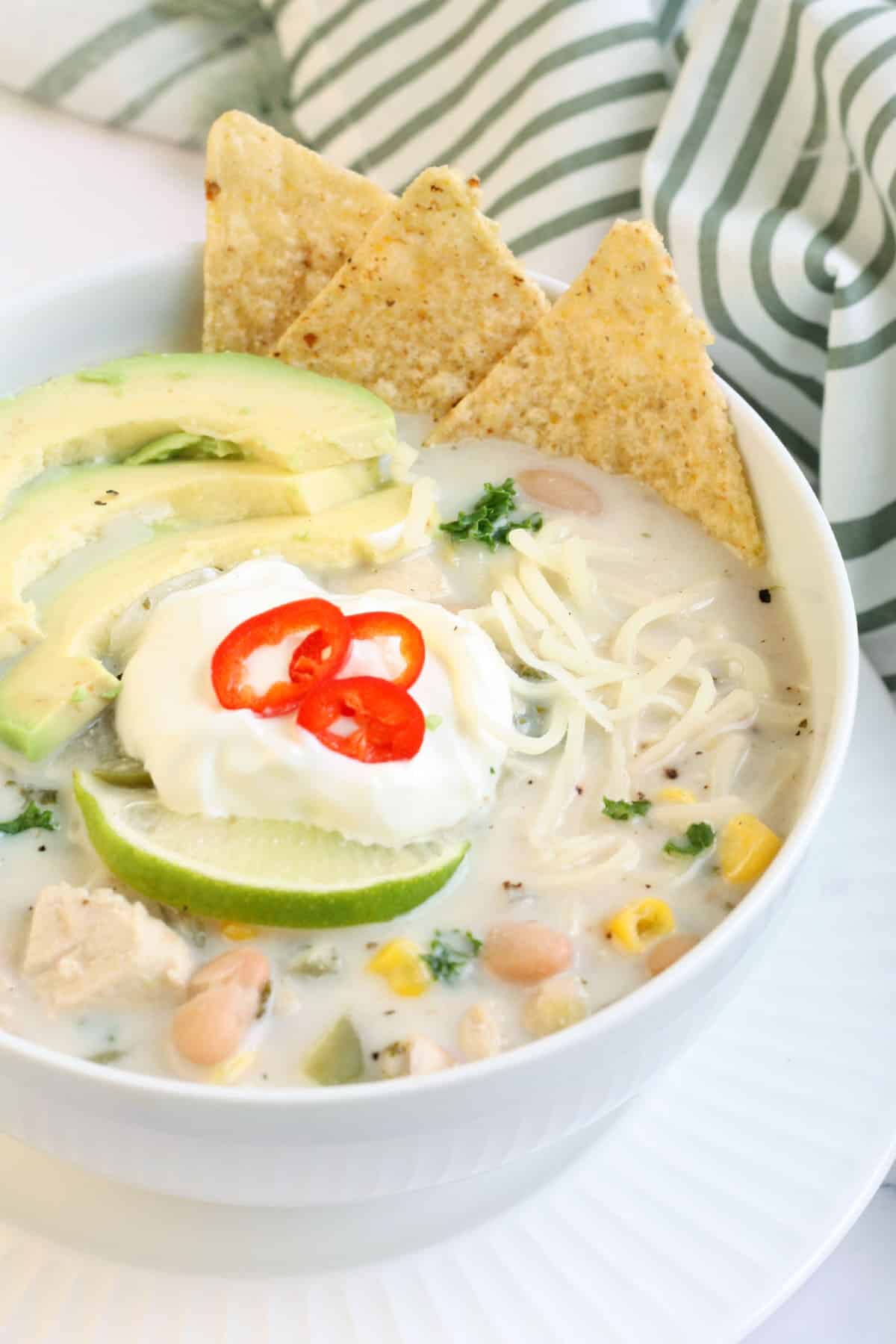 a bowl of white chicken chili topped with avocado, sour cream and tortilla chips