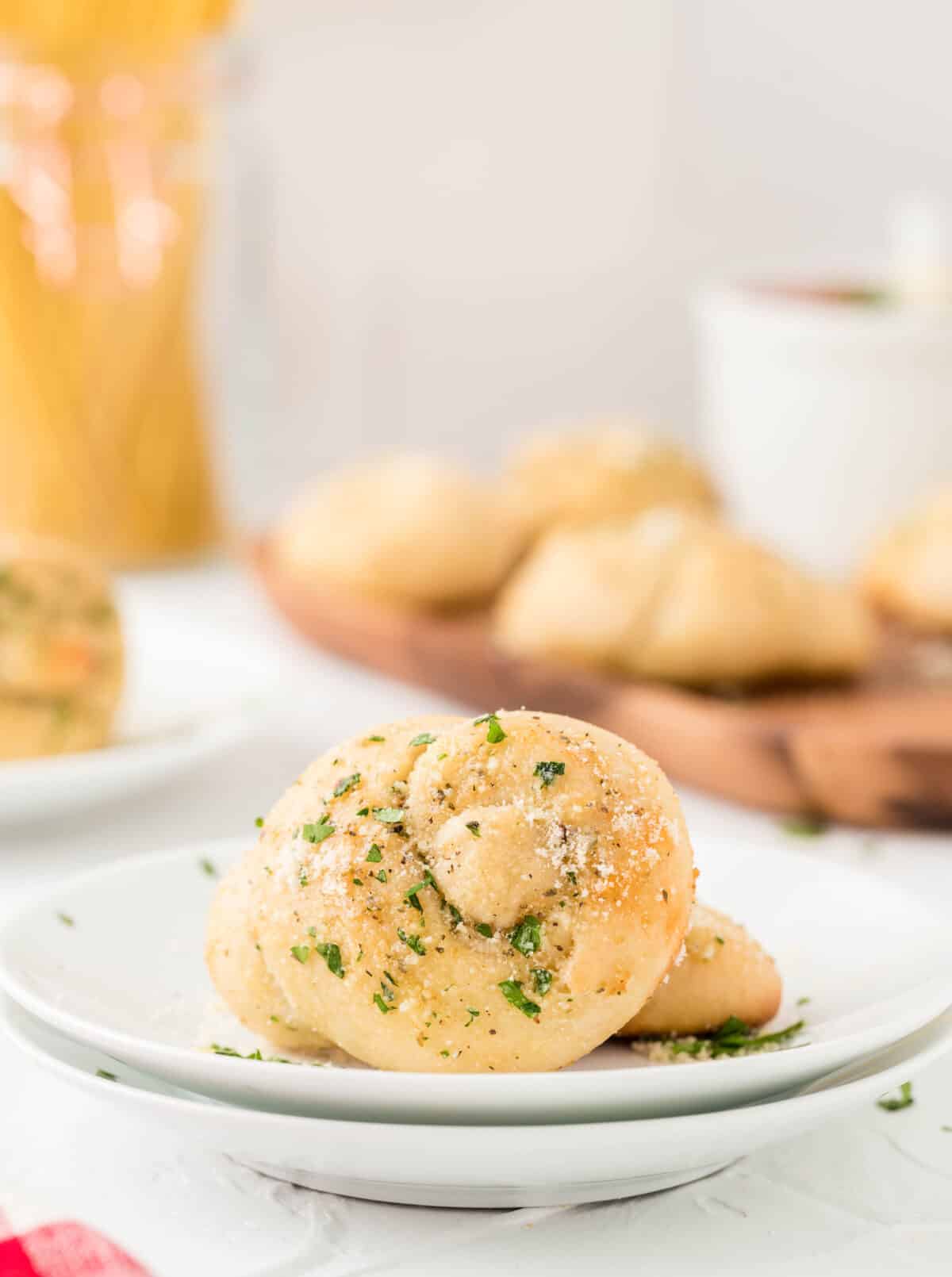 garlic knot on a white plate with garlic knots in the background on a wood cutting board