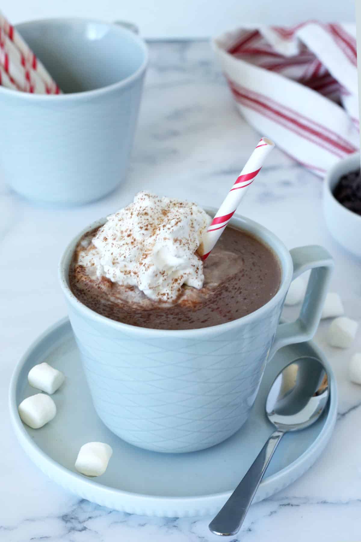 hot chocolate in a blue mug with whipped cream and a striped straw