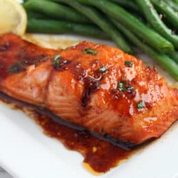 honey garlic salmon on a white square plate with green beans and a lemon slice