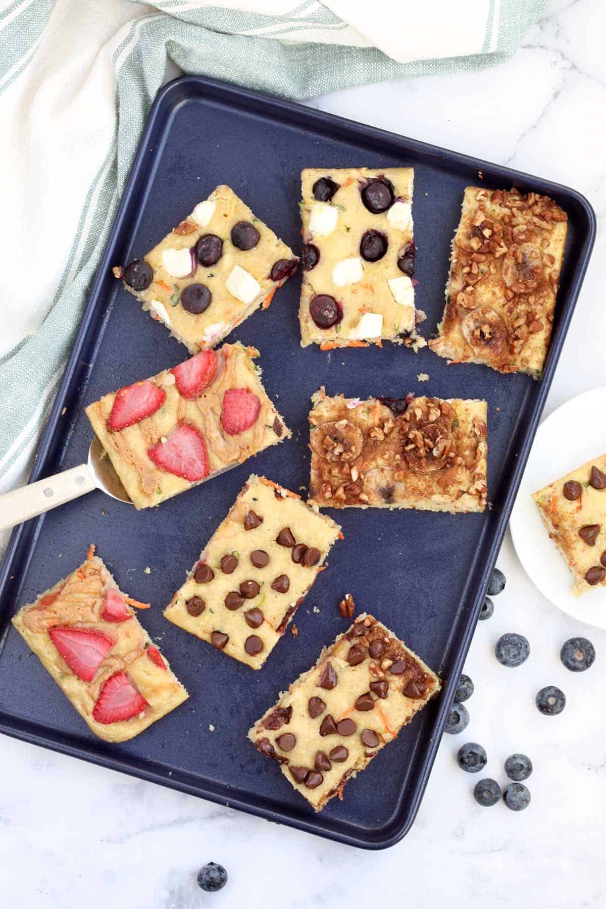 sheet pan pancakes topped with strawberries, chocolate chips, bananas, blueberries, and cream cheese.