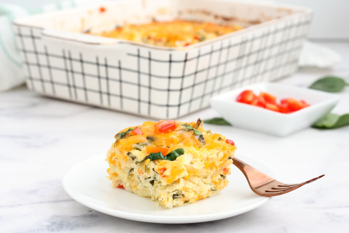 a plate of hashbrown breakfast casserole with peppers and spinach in the background