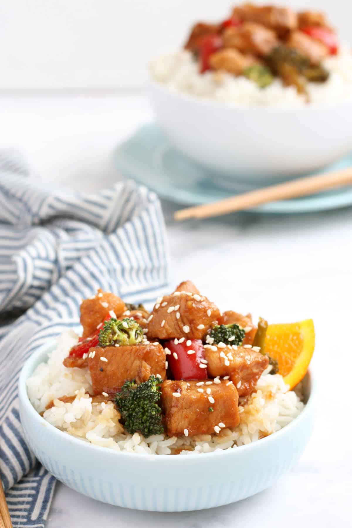 crockpot orange chicken served over rice and topped with sesame seeds in a blue bowl