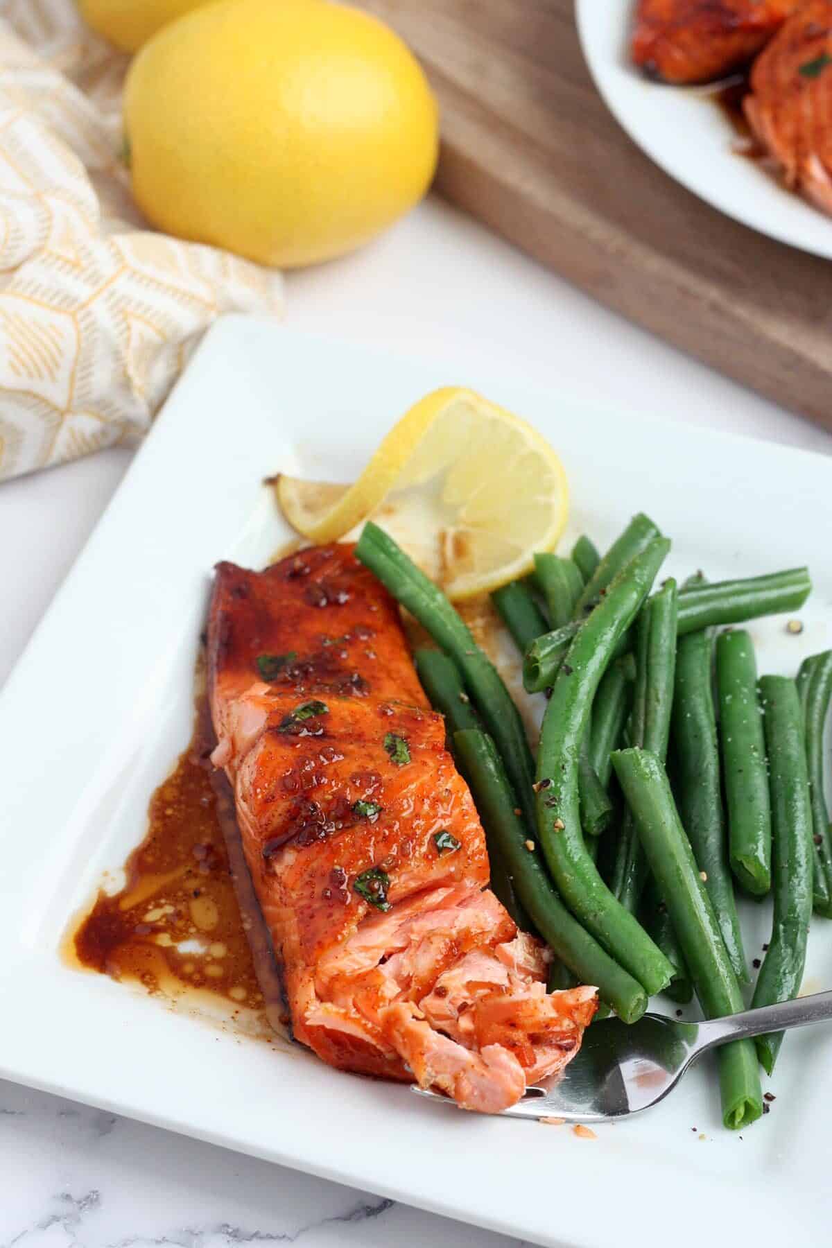 honey garlic salmon fillet with green beans on the side and a wedge of lemon