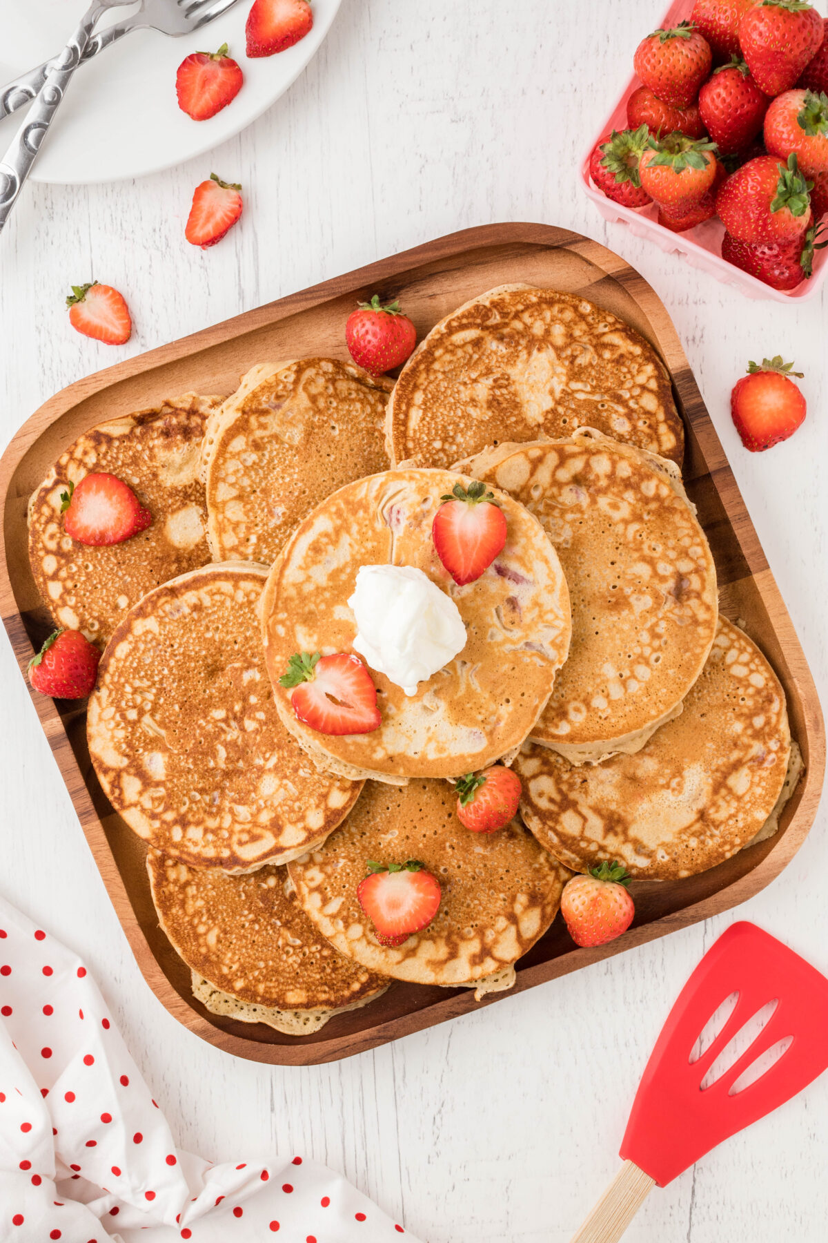 a wooden platter topped with a stack of strawberry pancakes