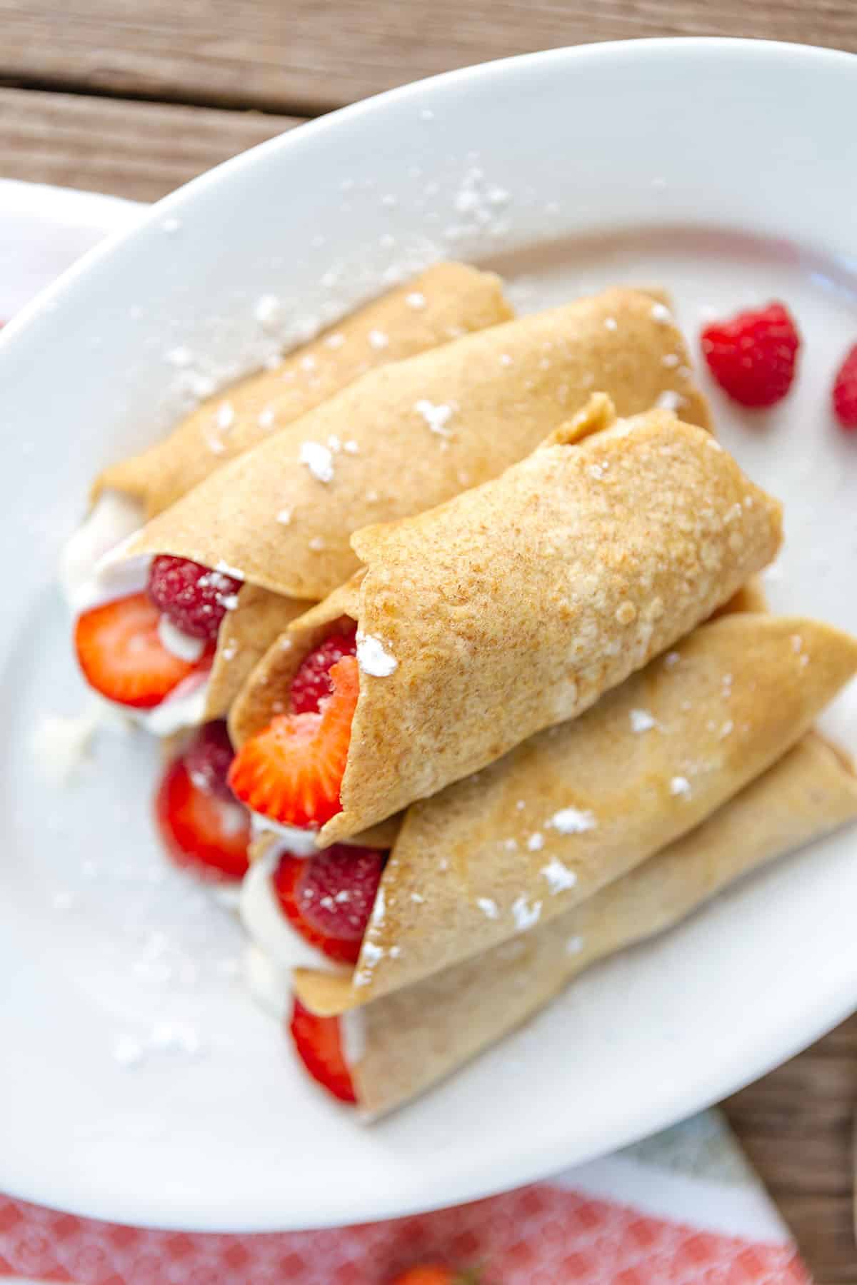 overhead view of strawberry crepes filled with fresh strawberries and raspberries and a cream filling on a white plate