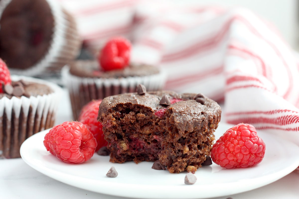 a chocolate bran muffin with a bite taken out on a plate with raspberries