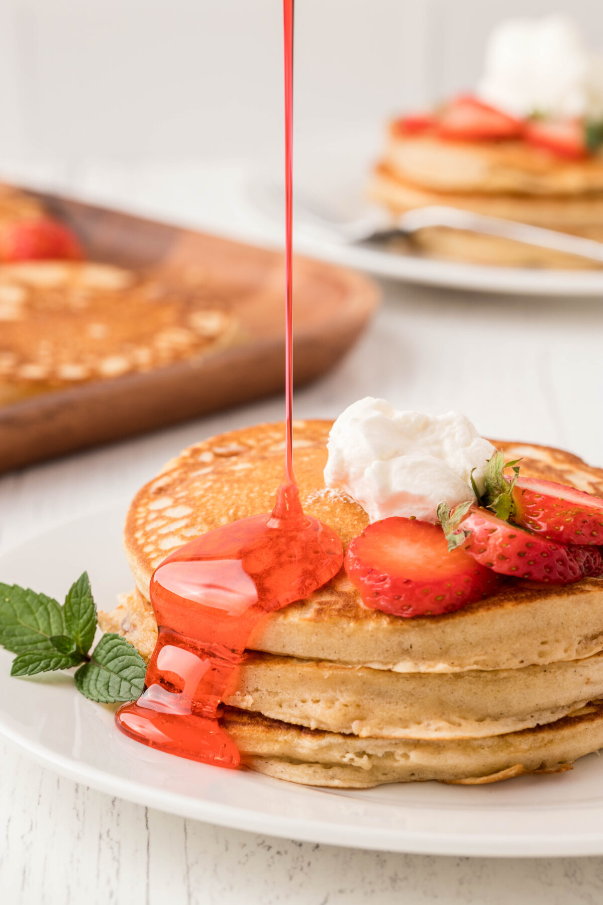 a stack of strawberry pancakes topped with whipped cream and drizzled with strawberry syrup