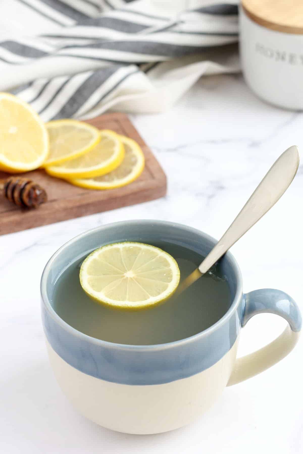a mug of honey lemon drink in a blue mug with a slice of lemon floating on top