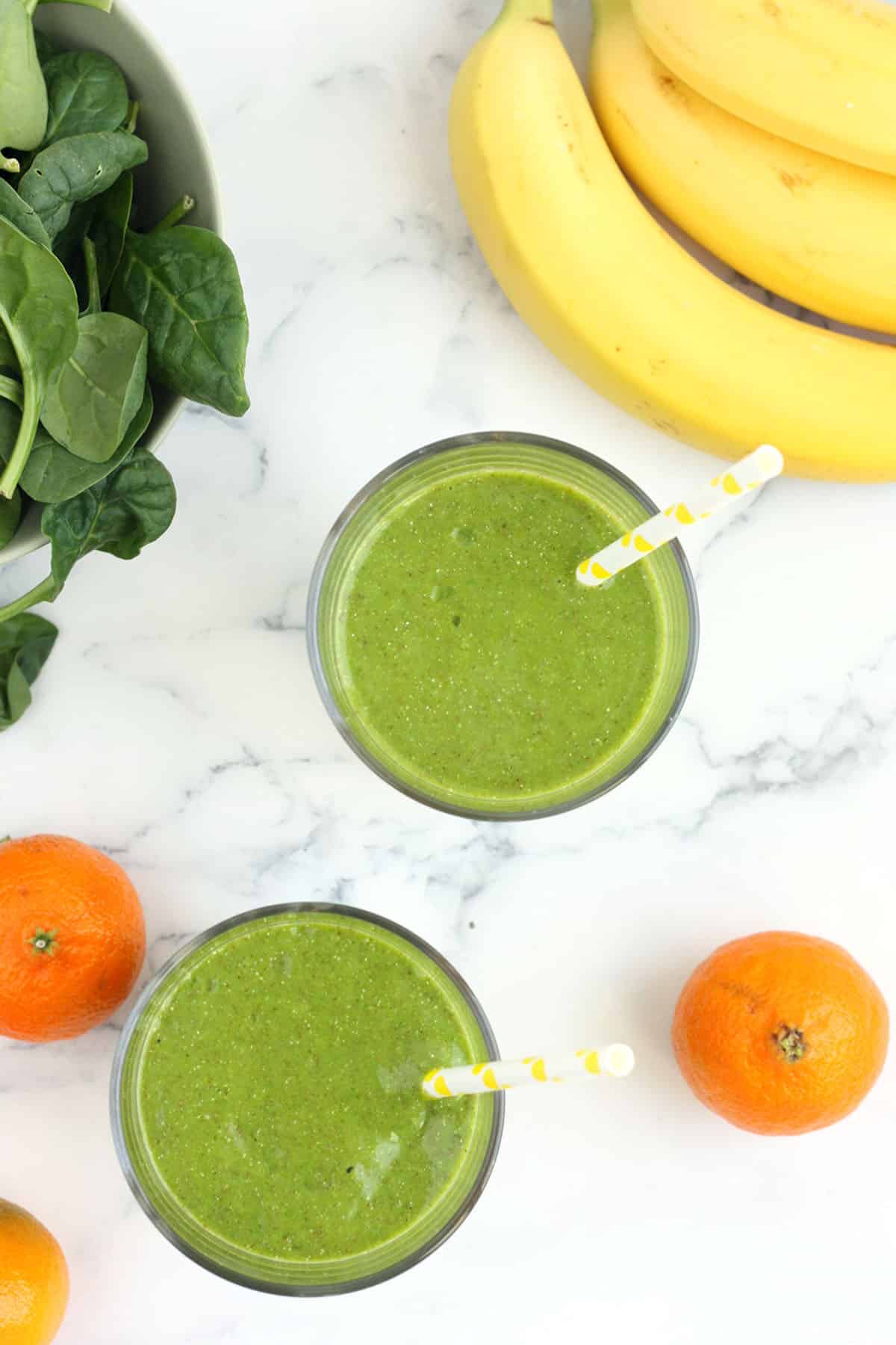 an overhead shot of green smoothies, bananas, spinach, and oranges