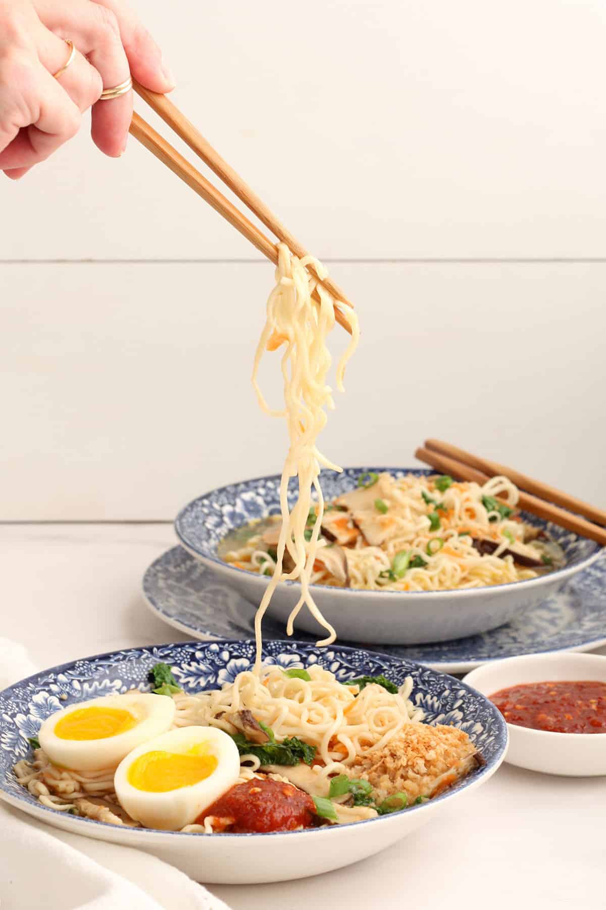 someone using chopsticks to get a bite of homemade ramen noodles out of a large blue bowl
