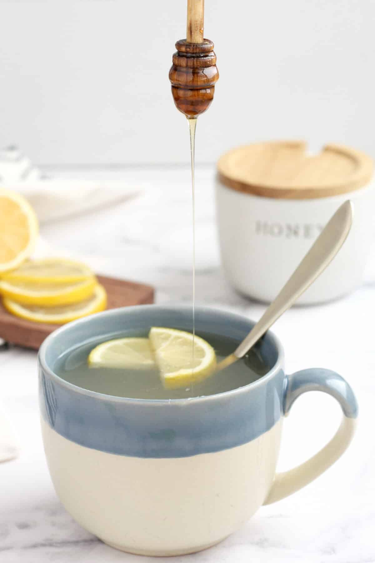 a mug of honey lemon tea with lemon slices and a drizzle of honey