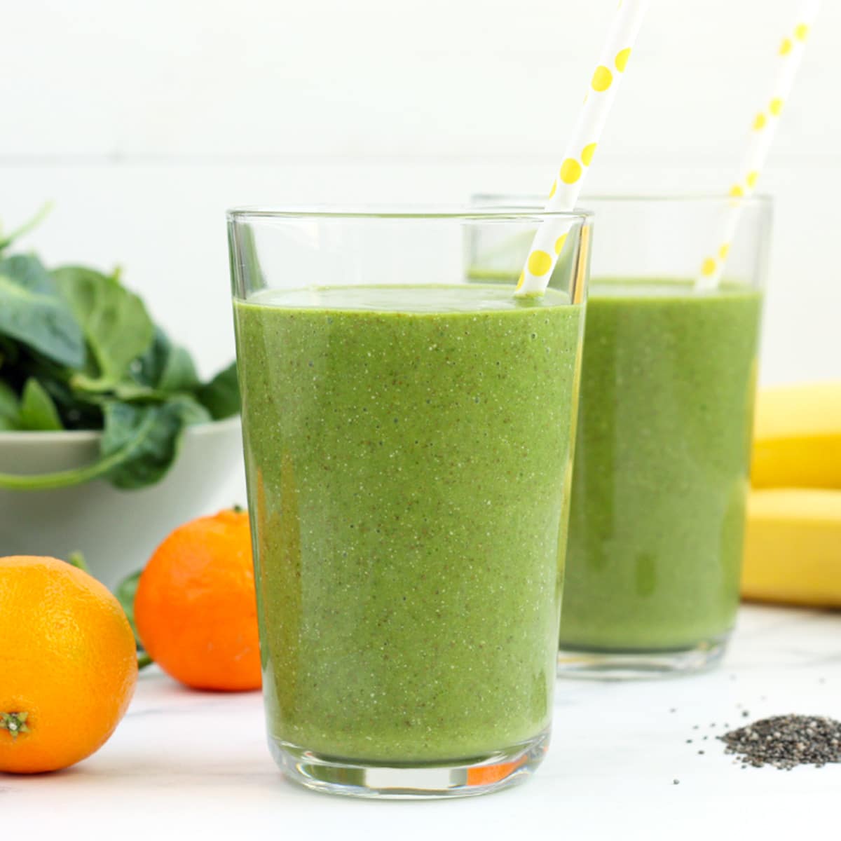 two green smoothies in glasses with paper straws