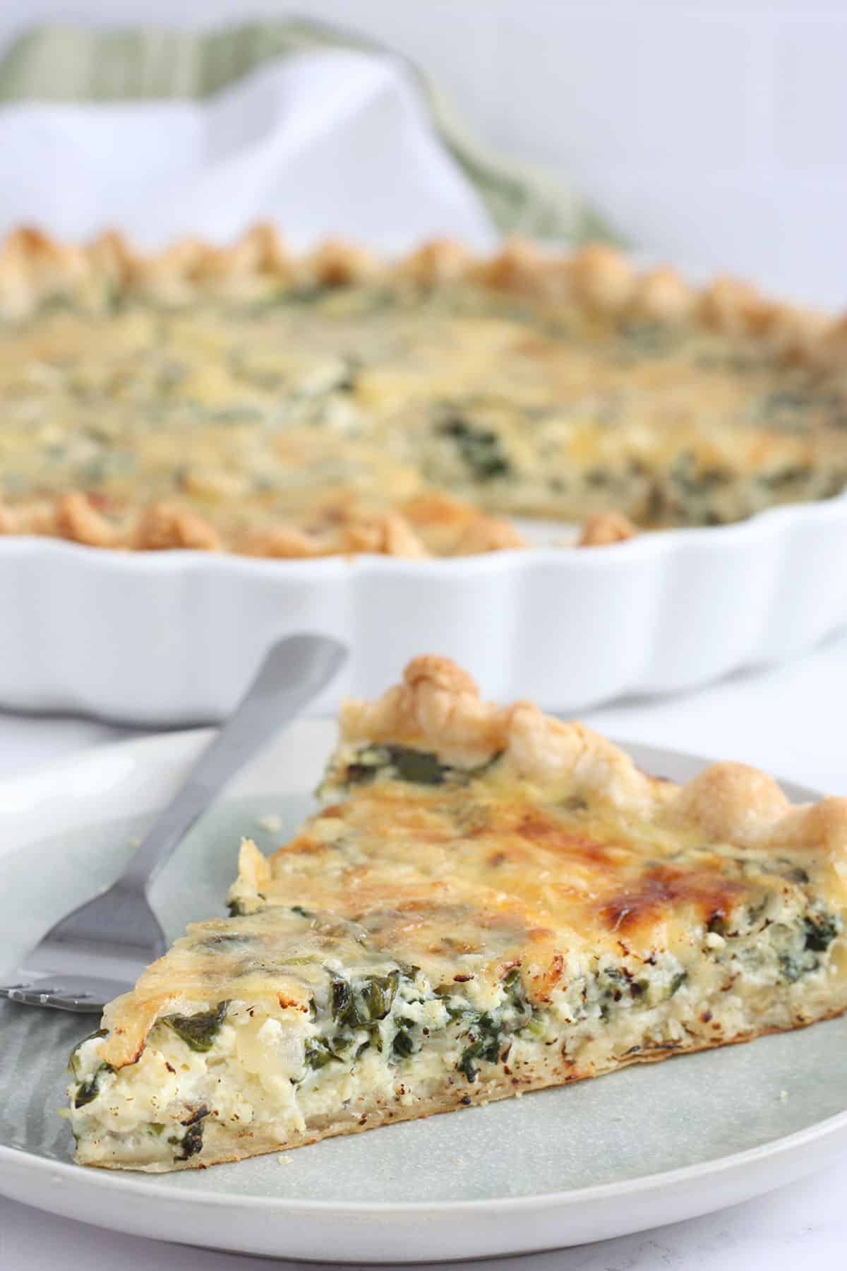 a slice of spinach quiche on a serving plate with a fork