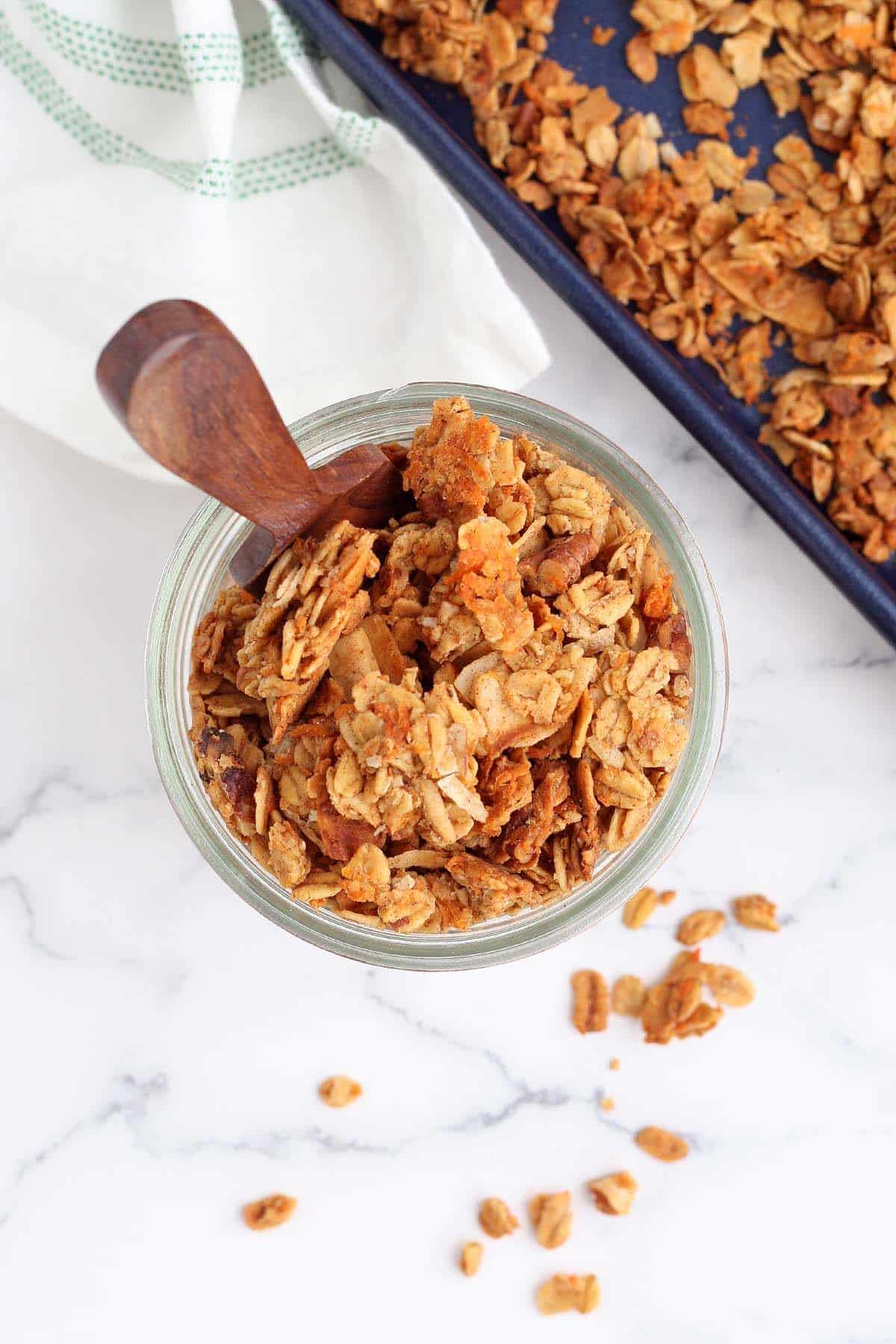 an overhead shot of carrot cake granola in a mason jar with a wooden scoop