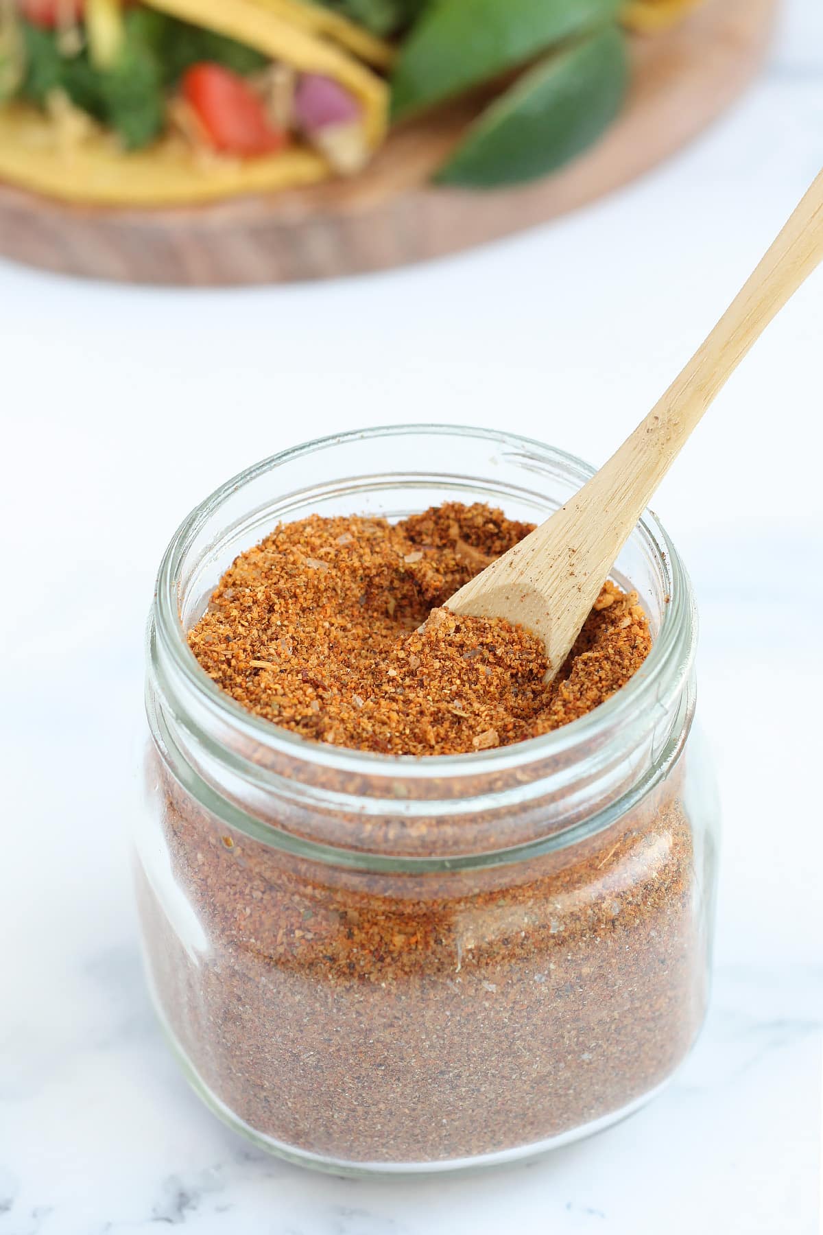 a small glass mason jar filled with taco seasoning with a wooden spoon