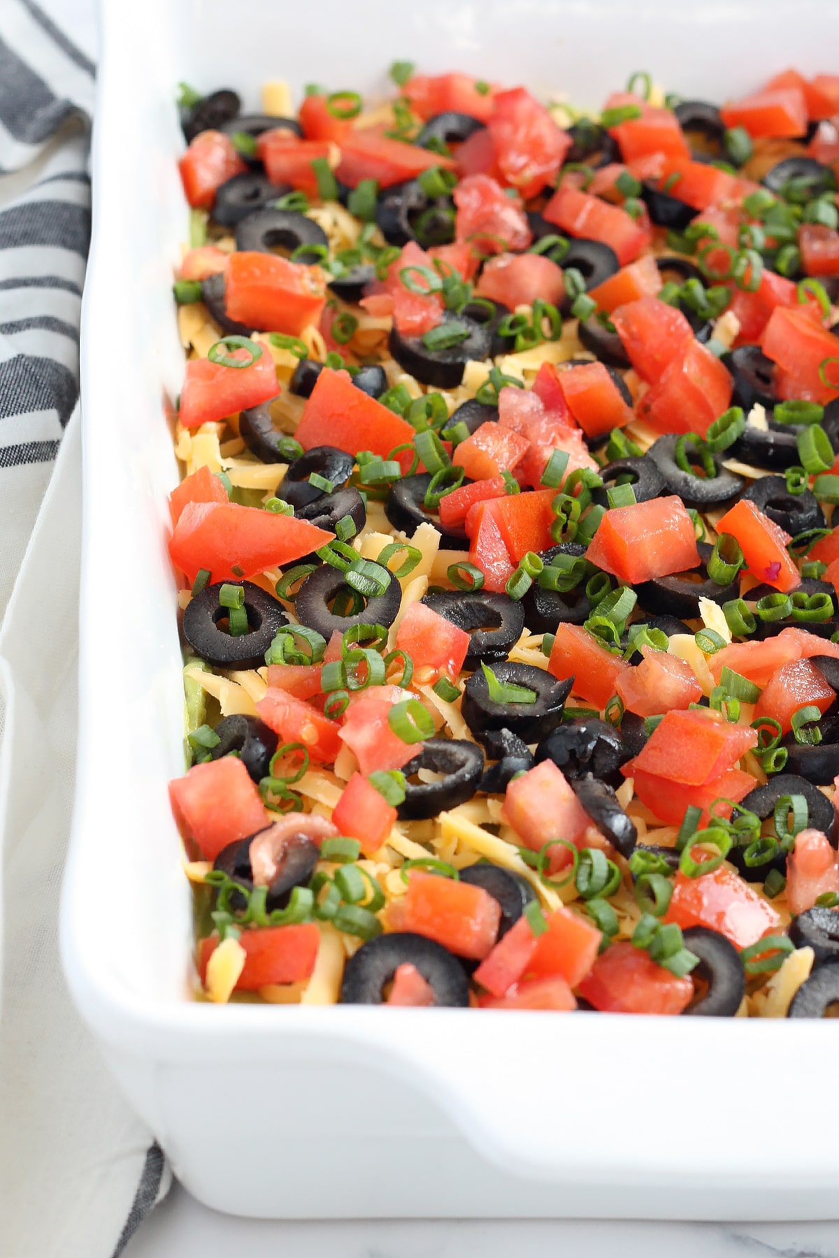 seven layer bean dip in a casserole dish topped with olives and diced tomatoes
