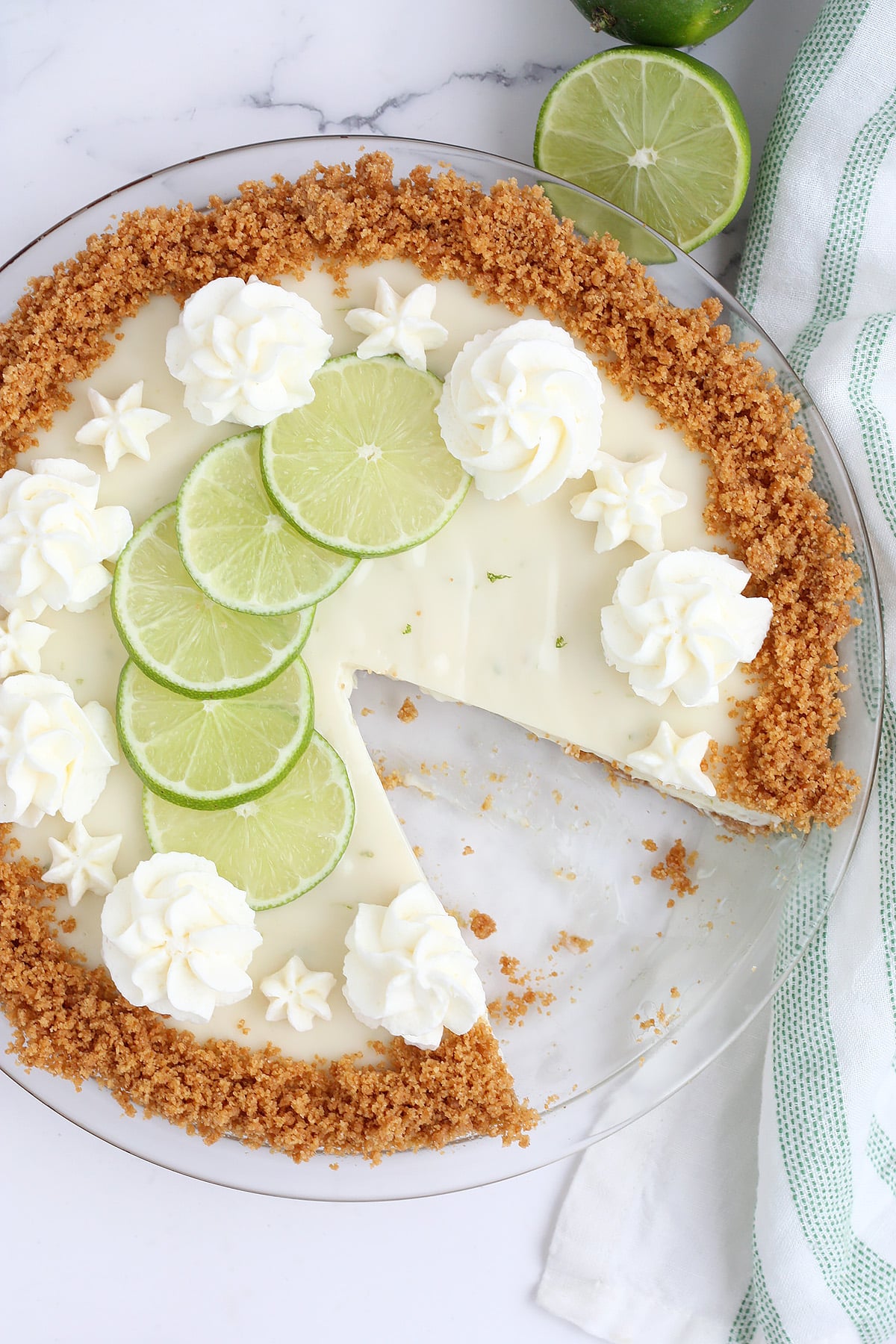 An overhead shot of key lime pie in a glass pie plate with a slice removed.