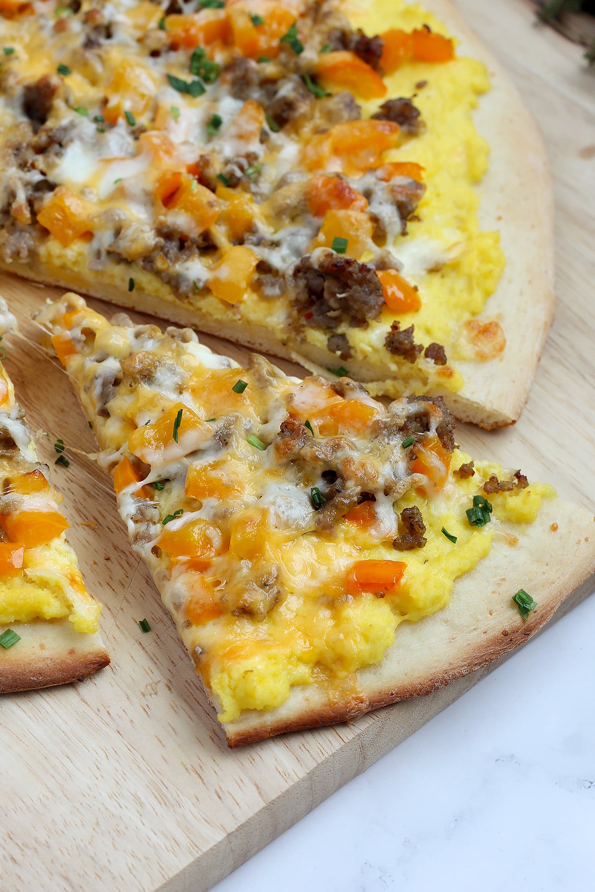 A close up slice of breakfast pizza on a wooden board.
