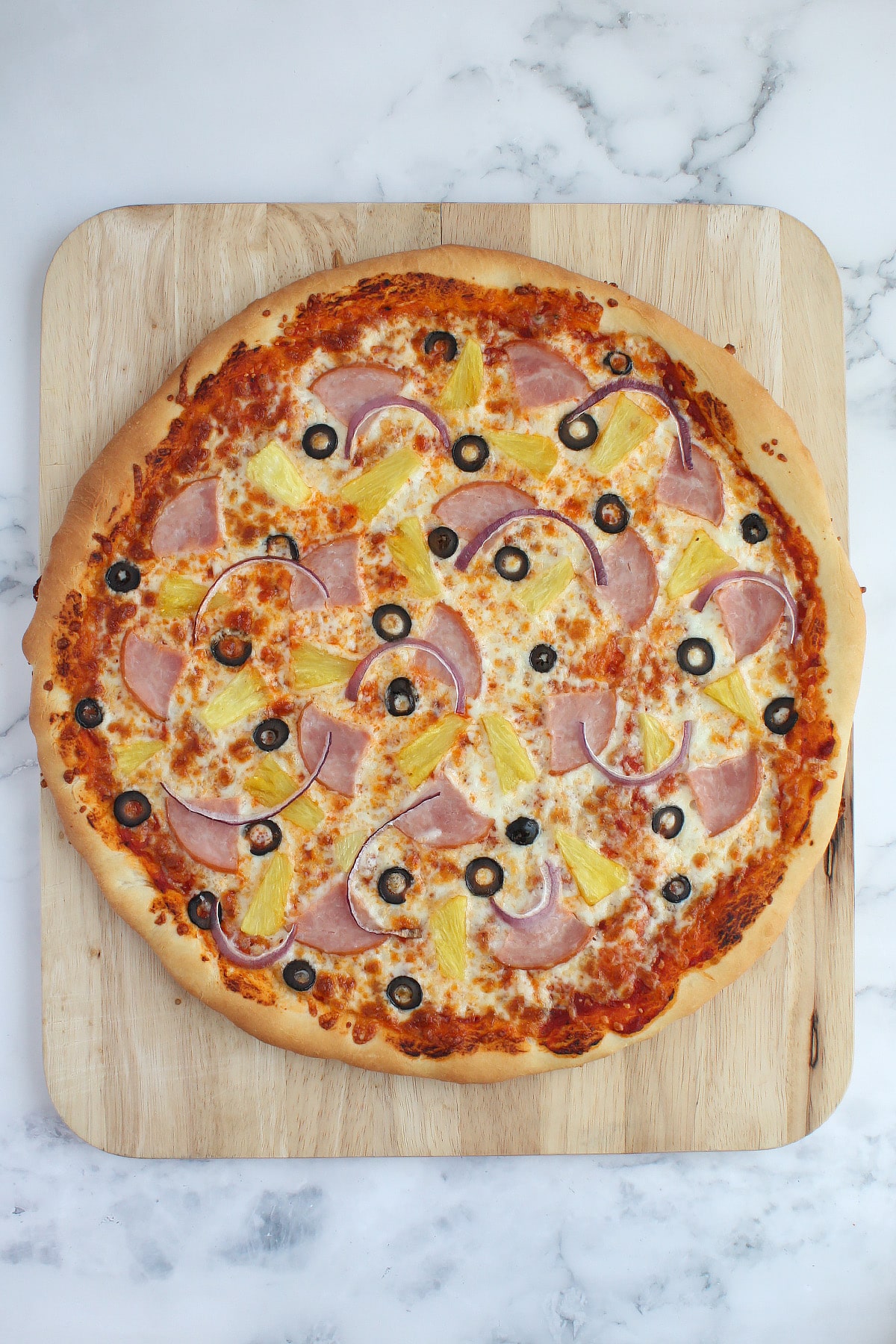 A homemade pizza topped with ham, pineapple, red onions and olives.